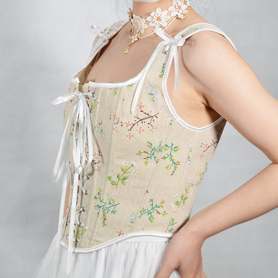 Elegancki top gorsetowy typu bustier z beżowym tłem i subtelnym wzorem kwiatowym. Posiada regulowane wiązanie z przodu i urocze kokardy na ramiączkach.