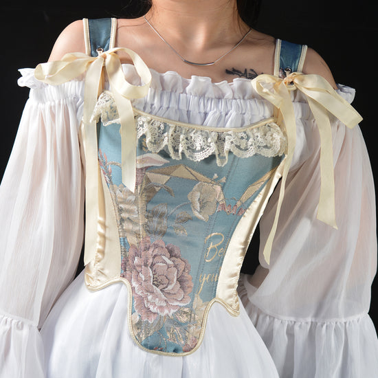Wiktoriański gorset top w kolorze niebieskim z delikatnym kwiatowym wzorem, ozdobiony koronką i uroczymi kokardkami, idealny do stylizacji vintage.